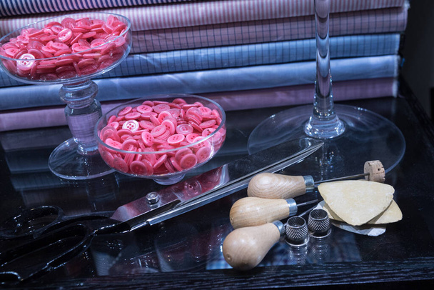 Tavolo sartoriale con attrezzi assortiti tra cui puntale, ditali, bottoni e gesso
 - Foto, immagini