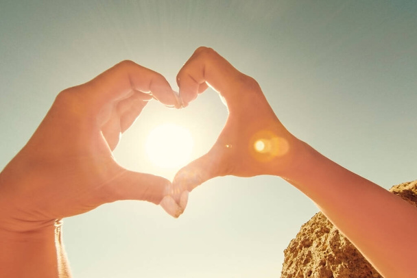 Vrouwelijke handen in de vorm van hart tegen de hemel passeren zonnestralen. - Foto, afbeelding