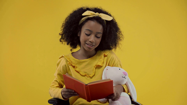 niño afroamericano feliz leyendo en voz alta aislado en amarillo
  - Metraje, vídeo