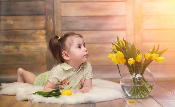 A small child with a bouquet of yellow tulips. A boy with a gift of flowers in a vase. A gift for girls on female holiday with yellow tulips on the floor - Zdjęcie, obraz