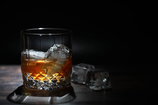 Un bicchiere di forte bevanda alcolica con ghiaccio sul bancone del bar in legno. Whisky con cubetti di ghiaccio. Bicchiere con una bevanda refrigerata. - Foto, immagini