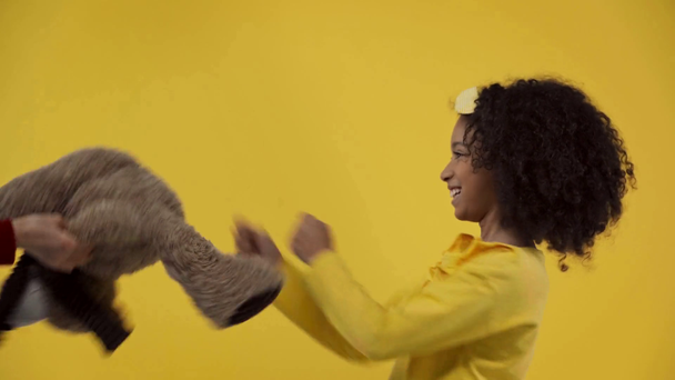 african american kid fighting with teddy bear isolated on yellow  - Кадри, відео
