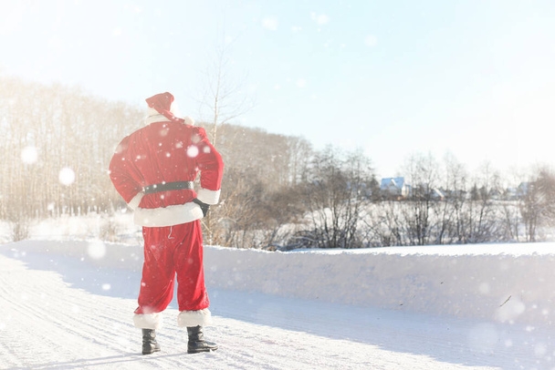 サンタ クロースでは、外から、贈り物を付属しています。ひげとめがねをかけて赤いスーツのサンタがクリスマスに道に沿って歩いています。父のクリスマスは、子供たちに贈り物をもたらす. - 写真・画像