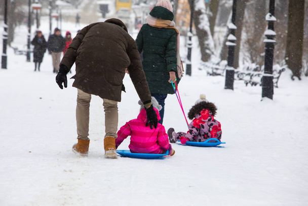 dzieci ślizgające się na zimowym wzgórzu w parku miejskim rodzice pchając zabawy - Zdjęcie, obraz