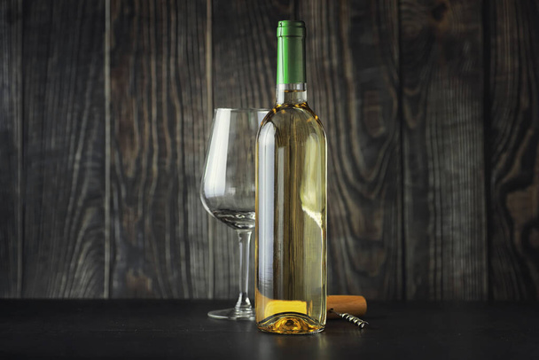 Прозрачная бутылка белого сухого вина на столе. Бокал белого вина на фоне деревянной стены
. - Фото, изображение