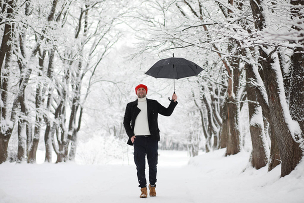 Muž na procházce v parku. Mladý muž s deštníkem pod zimním sněhem. - Fotografie, Obrázek