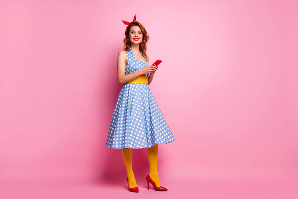 Full body profile photo of pretty beautiful lady hold telephone hands wear headband polka dotted dress red high-heels yellow stockings isolated pink color background - Fotografie, Obrázek