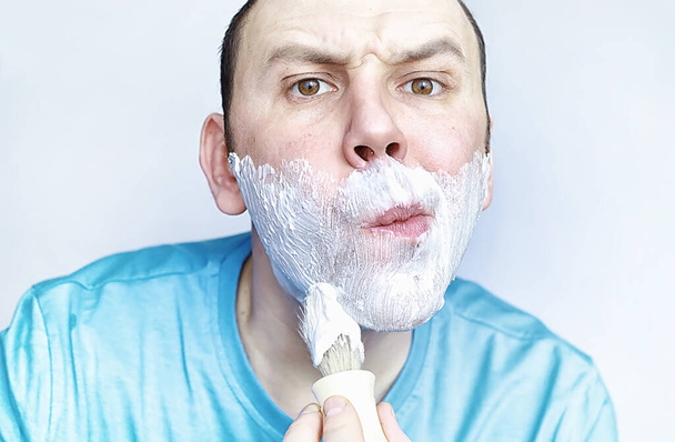A man shaves in front of a mirror. Shaving foam. Disposable razor. - Foto, imagen