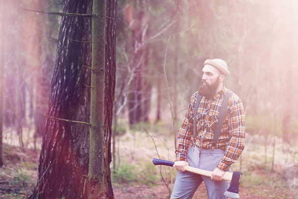 Бородатый дровосек с большим топором осматривает дерево перед срубкой.
 - Фото, изображение