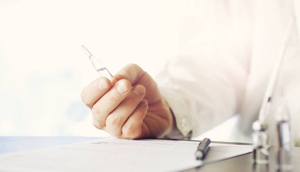 A man signs a medical document. Medical equipment on the table. Stethoscope and ampoules with syringes. Makes notes in office. Medical center. - 写真・画像