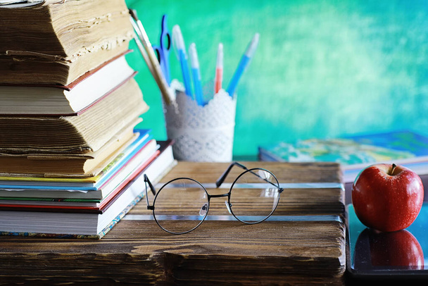 Education concept. A stack of textbooks and a book on the desk with glasses and computer. School breakfast apple and homework. - 写真・画像