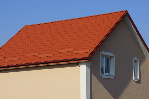 großes privates braunes Haus mit weißen Fenstern unter einem roten Ziegeldach vor blauem Himmel an einem sonnigen Tag - Foto, Bild