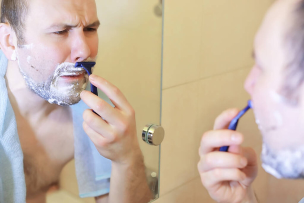 Egy férfi borotválkozik reggel munka előtt a mosdóban. - Fotó, kép