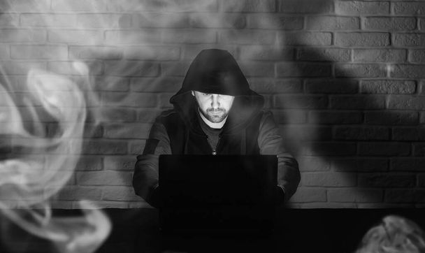 Fekete maszkos hacker és csuklyás az asztalnál a monito előtt. - Fotó, kép
