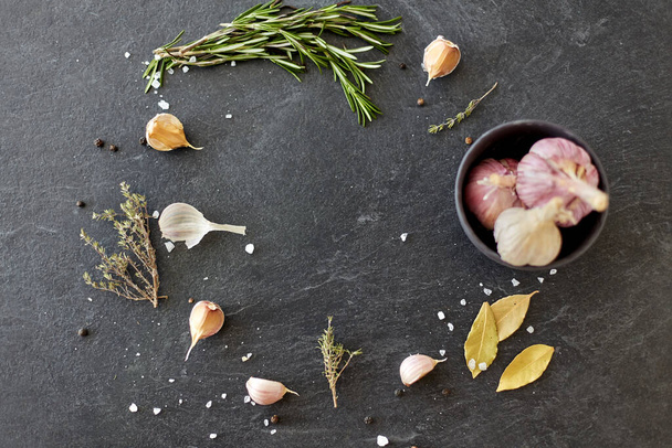 garlic in bowl and rosemary on stone surface - Zdjęcie, obraz