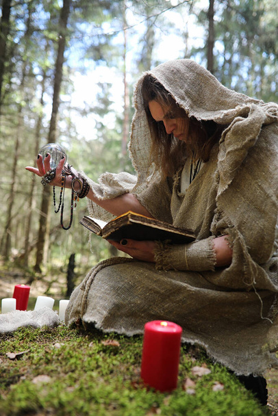 Een man in een soutane brengt een ritueel in een donker bos met een kristallen bol en Boo - Foto, afbeelding
