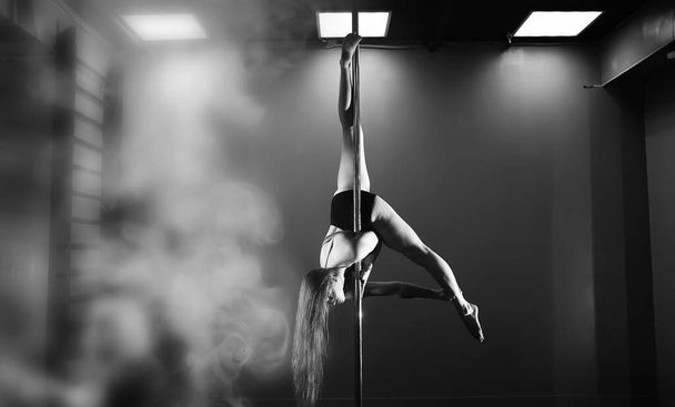 Girl doing exercises on a sports equipment. The dancer on the pylon in the studio. - Photo, Image