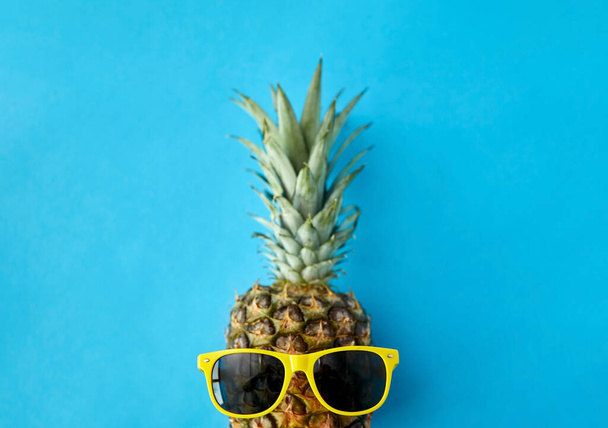 pineapple in yellow sunglasses on blue background - Foto, Imagen