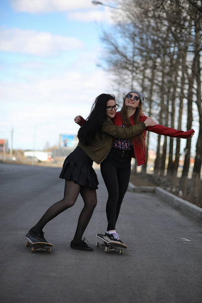Egy fiatal csípő lány lovaglás a gördeszka. Girls barátnőit egy séta a gördeszka város. Tavaszi sport az utcán egy gördeszka - Fotó, kép