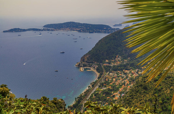 Vista panorâmica da costa mediterrânica, dos Alpes e das casas medievais da vila de Eze, na Riviera Francesa, França, com uma fronte embaçada de palmeiras
 - Foto, Imagem