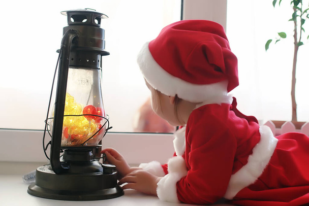 A child in the new year looks out the window. Children are waiting for Santa Claus. A child in Santa suit sits at the window - Photo, Image