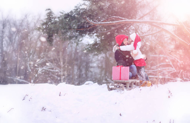 Wintermärchen fahren eine junge Mutter und ihre Tochter mit dem Schlitten durch den Wald. Ein Mädchen auf einem Schlitten mit Geschenken am Vorabend des neuen Jahres im Park. zwei Schwestern spazieren im Neujahrspark und fahren Schlitten mit Geschenken - Foto, Bild