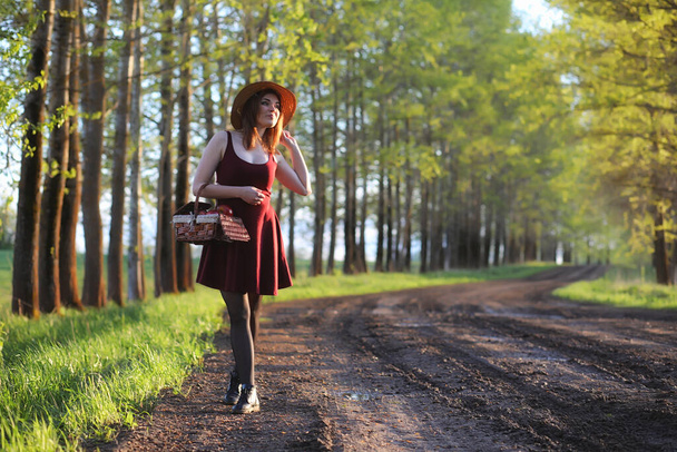 Una chica con sombrero en un paseo por el parque. Una chica con una cesta camina en primavera. Chica está caminando por el camino al atardecer - Foto, Imagen