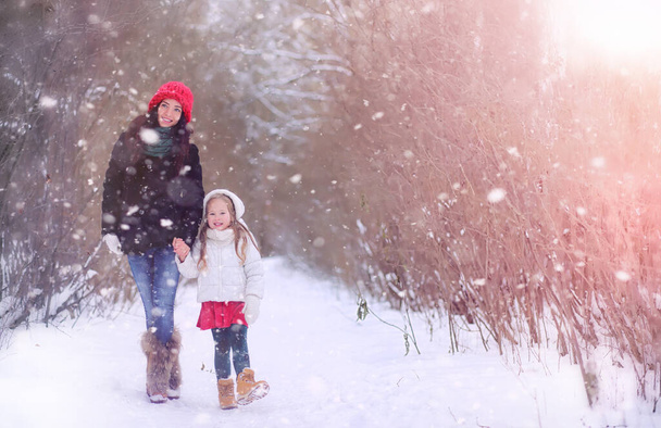 Zimní pohádka, mladá matka a její dcera jezdí na saních v lese. Dívka na saních s dárky v předvečer nového roku v parku. Dvě sestry se procházejí v novoročním parku a jezdí na saních s dárky - Fotografie, Obrázek