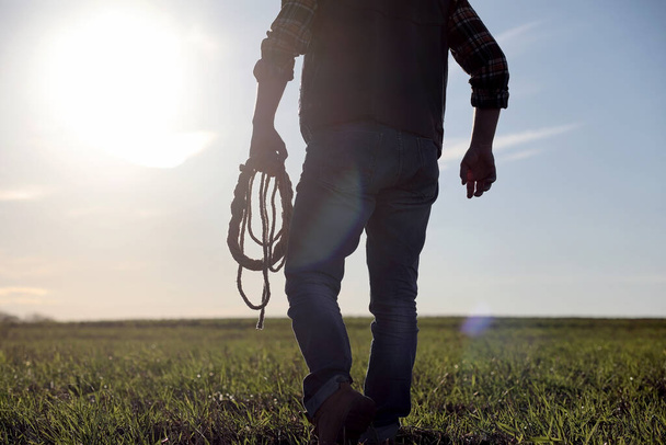 Un sombrero de vaquero y un loso en el campo. Un granjero americano en un campo con un sombrero vaquero y un loso. Un hombre está caminando por el campo con un sombrero - Foto, imagen