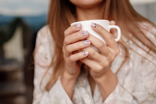 Bir kızın elleri beyaz bir fincanı kahve ya da çayla tutuyor.. - Fotoğraf, Görsel