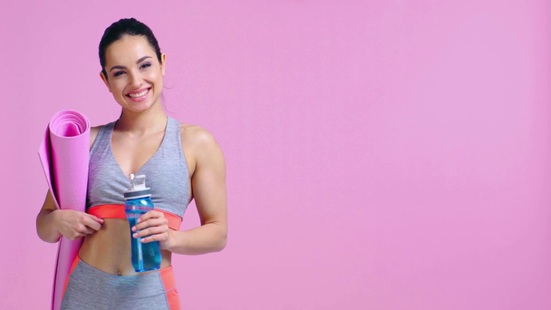 happy girl with sports bottle and fitness mat isolated on pink  - Footage, Video