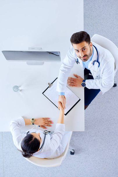 Flache Lage, Draufsicht. Professionelle arabische Ärzte im Krankenhaus mit Tabletten am Tisch sitzend und Hände schüttelnd. Gruppe von Ärzten im Krankenhaus  - Foto, Bild