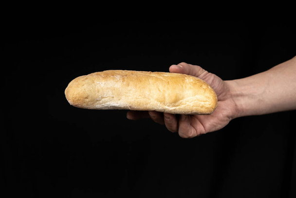 Fresh bread ciabatta in the male hand on black background. - Photo, Image