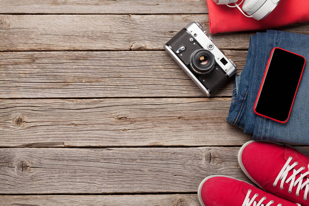 Одяг та аксесуари. Кросівки, джинси, навушники та смартфон. Міське вбрання для повсякденних або туристичних відпусток на дерев'яному тлі з копіювальним простором. Вид зверху плоский лежав
 - Фото, зображення