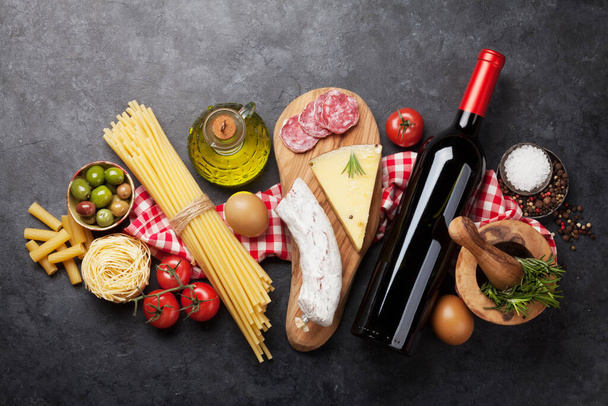 Italian cuisine food ingredients. Pasta, cheese, salami, olives and wine. Top view flat lay on stone table - Photo, Image