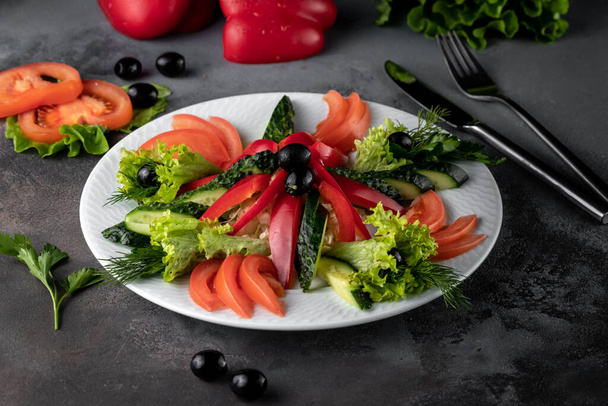 tomato, bell pepper, cucumber slices, lettuce and thyme on white plate, served on grey cement background in rustic style with copy space, sliced raw assorted vegetables in food restaurant, side view - Photo, Image