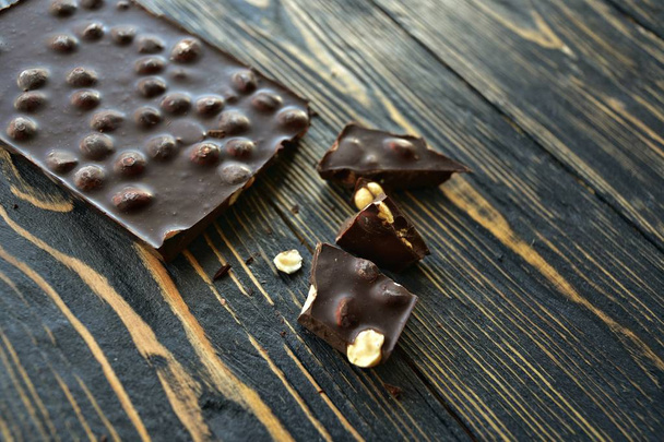 Sztabka ciemnej czekolady z orzechami laskowymi i kawałkami czekolady na ciemnym drewnianym tle. Widok boczny. - Zdjęcie, obraz