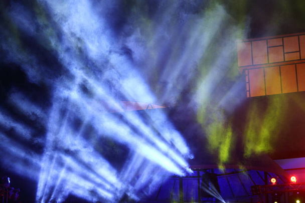 コンサートやファッションショーで、黄色の青の色で建設光ビーム線の下に照明を移動煙とステージランプ - 写真・画像