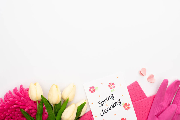 top view of tulips and pink cleaning supplies near spring cleaning card on white background - Zdjęcie, obraz