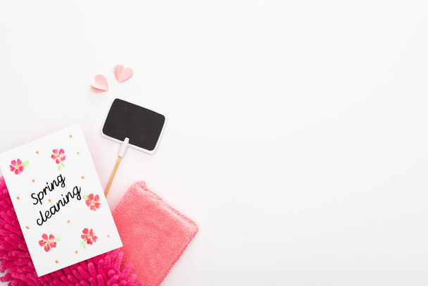 πάνω όψη του ροζ προμήθειες καθαρισμού, καρδιές και άδειο σημάδι κοντά στην κάρτα καθαρισμού άνοιξη σε λευκό φόντο - Φωτογραφία, εικόνα