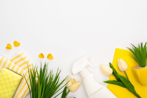top view of spring tulips and green plants near yellow cleaning supplies and hearts on white background - Photo, Image