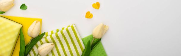 vista superior de los tulipanes de primavera, suministros de limpieza verdes y amarillos con corazones sobre fondo blanco, plano panorámico
 - Foto, Imagen