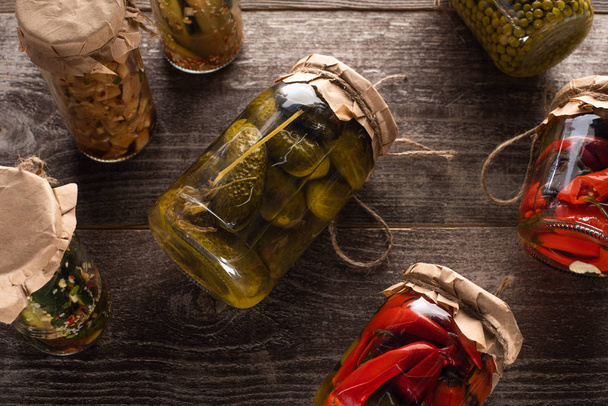 top view of homemade tasty pickles in jars on wooden table - Zdjęcie, obraz