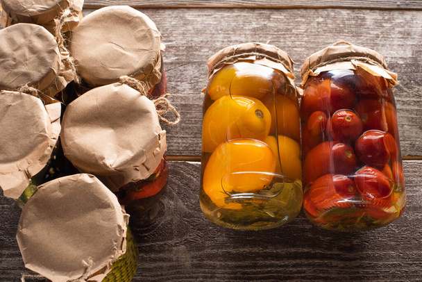 top view of homemade tasty canned red and yellow tomatoes near jars on wooden table - Photo, Image