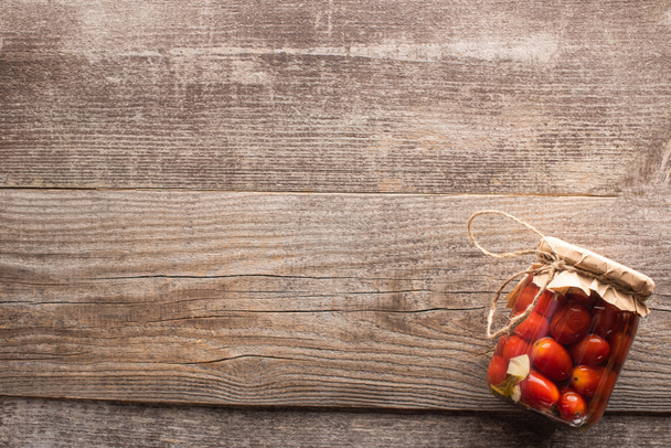 сверху вид на красные домашние вкусные маринованные помидоры в банке на деревянном столе
 - Фото, изображение