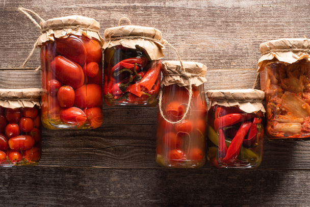 vrchní pohled na červené domácí chutné okurky ve sklenicích na dřevěném stole - Fotografie, Obrázek