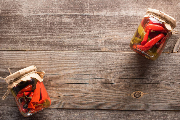 сверху вид на красный домашний вкусный маринованный перец чили в банках на деревянном столе
 - Фото, изображение