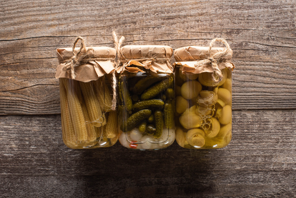 top view of delicious homemade tasty pickled cucumbers, corn and mushrooms on wooden rustic table - Foto, immagini
