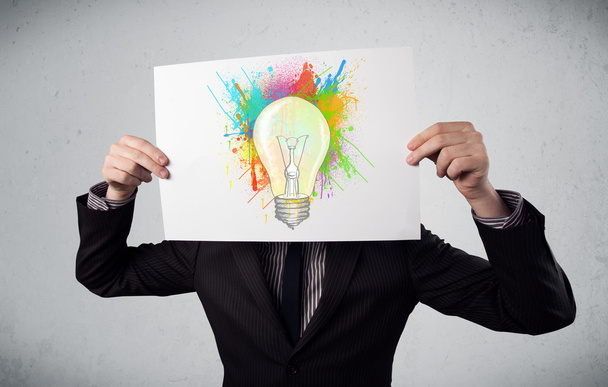 επιχειρηματίας που κρατά ένα χαρτόνι με πιτσιλιές χρωμάτων και lightbul - Φωτογραφία, εικόνα