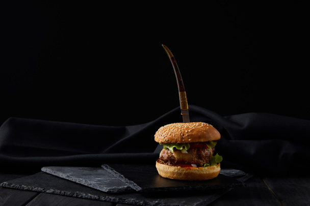 delicious burger on black cutting boards pierced by knife isolated on black - Photo, Image